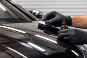Professional car detailing technician applying ceramic coating on a black car to protect and enhance exterior paint.